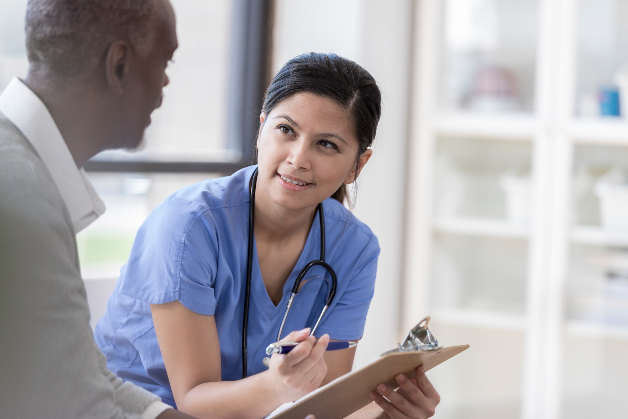 Smiling female nurse in blue scrubs shows patient a clipboard